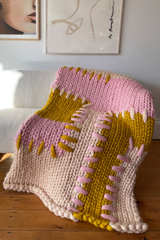 Handmade cream, pink and mustard colour block super chunky knitted blanket with thick patchwork stitching, on boucle sofa